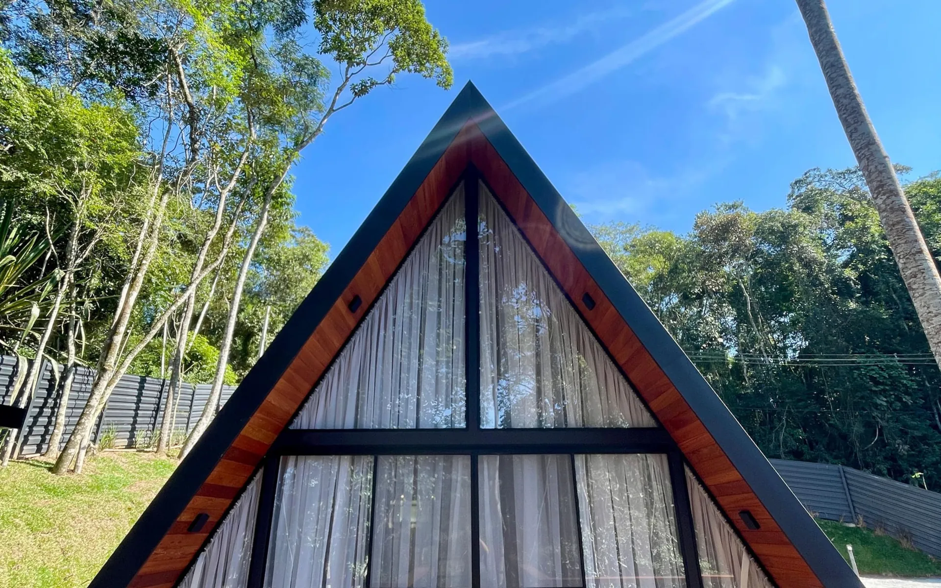 Cabana Bio de dia: a fachada A-frame de vidro e o deck de madeira, cercados pela mata atlântica